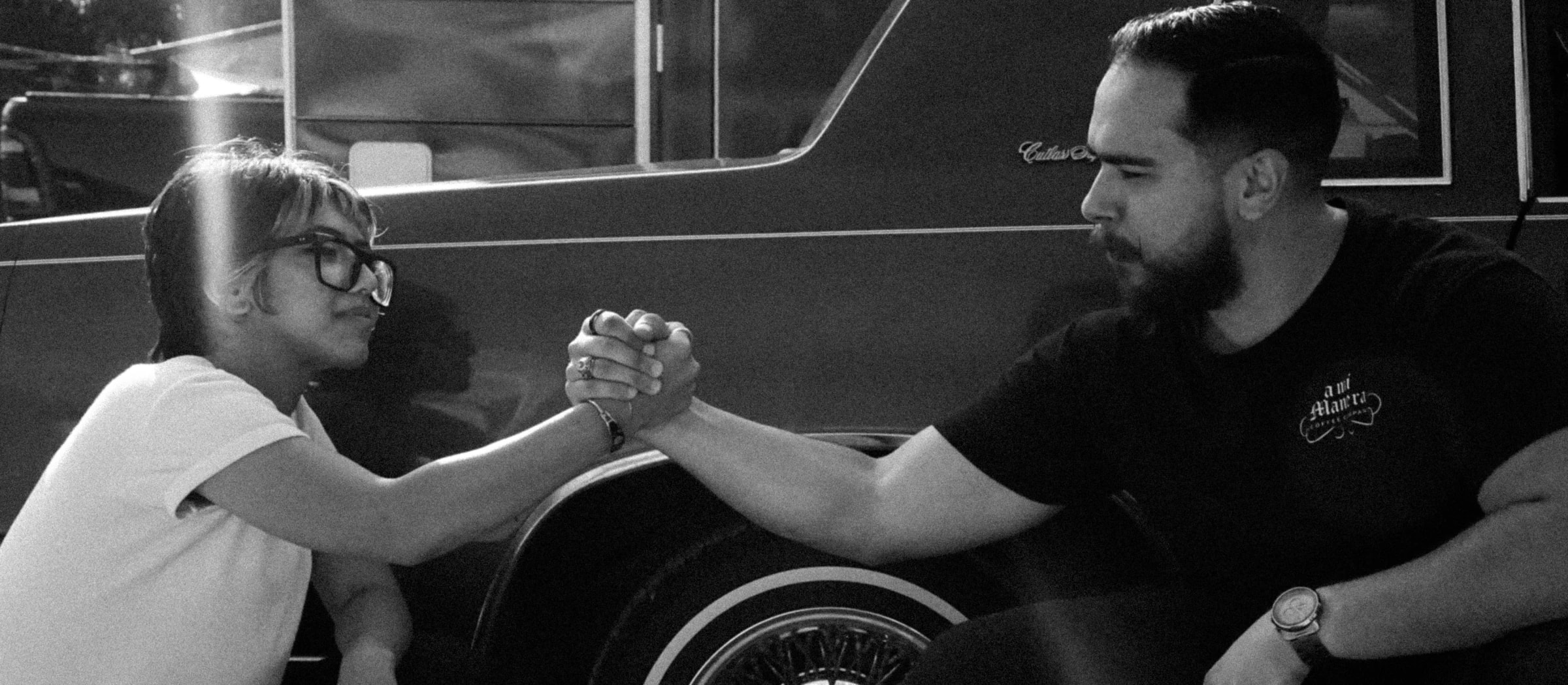 Tío and sobrina clasping hands in front of a lowrider